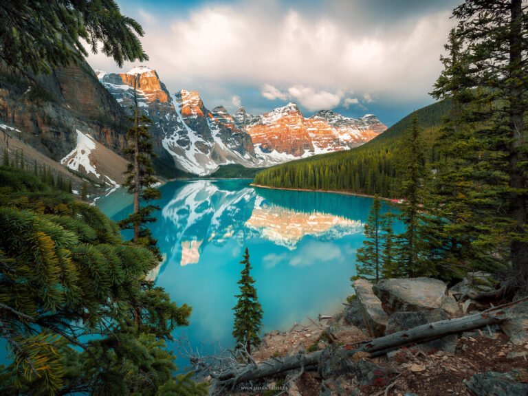 Moraine Lake at sunrise in Banff National Park in Canada framed by green fir trees with alpenglow