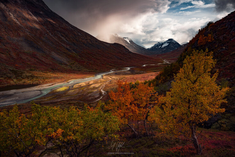 Epic autumn landscape in Jotunheimen National Park in Norway with fascinating light and shadow and colorful alpine landscape with different colored gnarled birch trees in the foreground