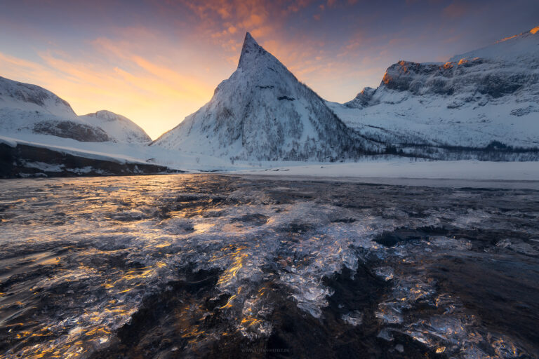 Pointed mountain in Ersfjord on Senja in northern Norway during an icy wintry sunrise with ice crystals in the foreground