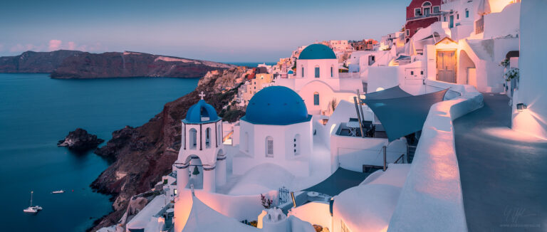 Blick über die weiße Stadt Oia auf Santorini in der Morgendämmerung. Bekannter Aussichtspunkt mit den drei blauen Kuppeln.