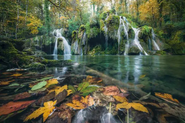 La Cascade des Tufs im französischen Jura im Herbst  in zauberhafter Stimmung mit Herbstlaub im Vordergrund