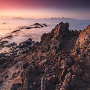 Morning view from the Cape Verde island of Santo Antao towards the island of Sao Vicente in the background with lava rocks in the foreground.